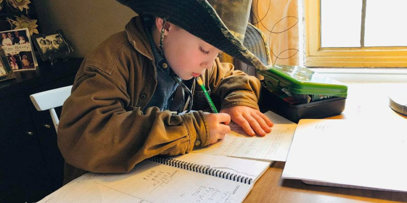 Student in a cowboy hat working at a table on school work