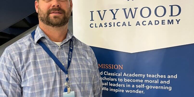 Picture of Ivywood Classical Academy Dean of Students Ben Ransier in front of an Ivywood branded standing-poster.